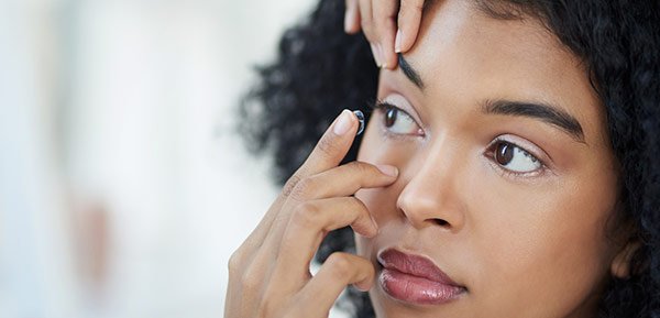 Young woman holding her eye open to place a contact in