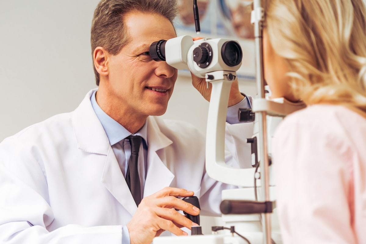 Doctor in lab coat doing an eye examination on a blond woman.