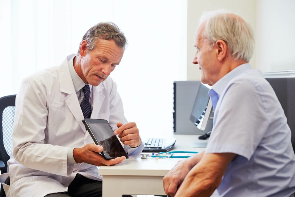 Male doctor and male patient sitting in an office where the doctor is showing the patient something on a tablet