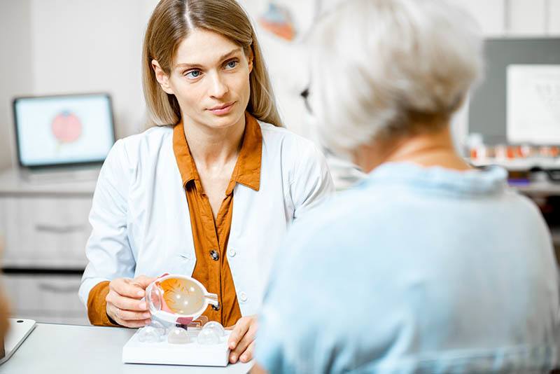 Doctor in lab coat showing a woman a model of an eyeball at a desk