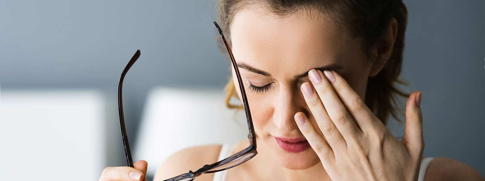 A woman holding her glasses while rubbing her eye