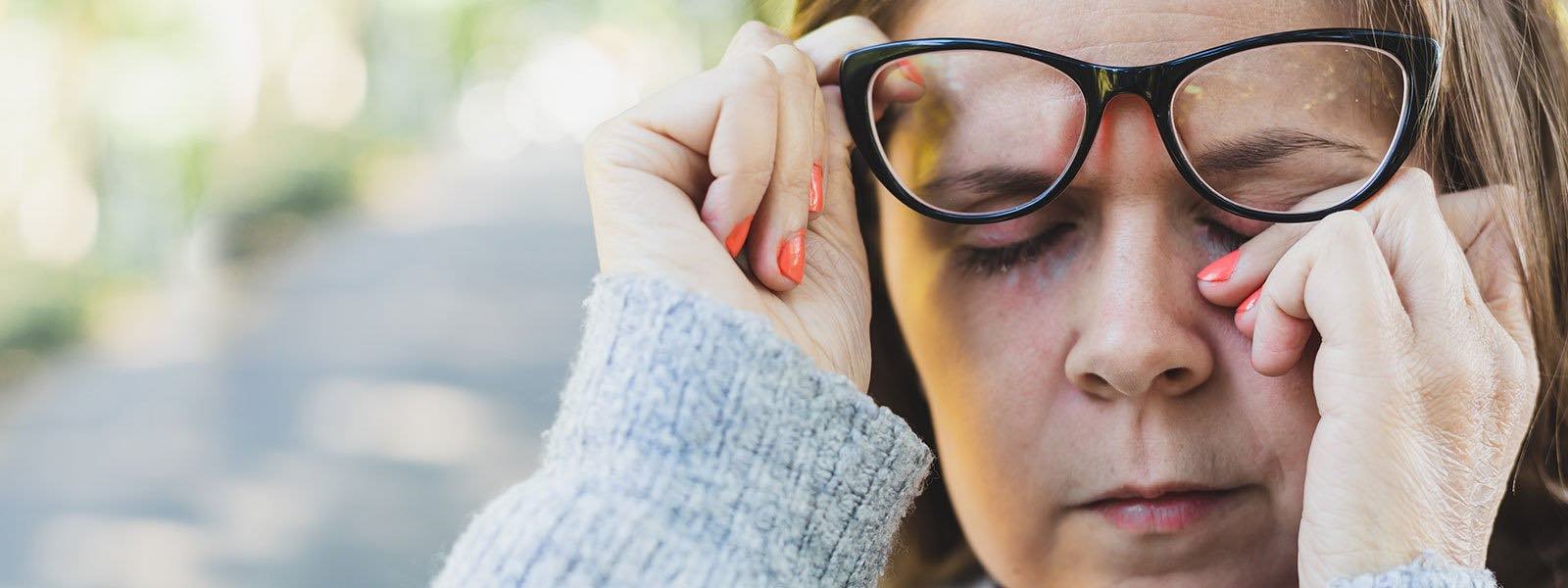 lady rubbing her eyes with her hands while raising her glasses